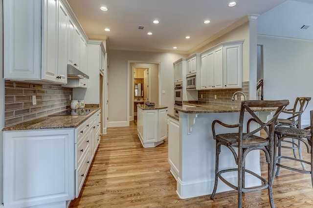 kitchen featuring kitchen peninsula, appliances with stainless steel finishes, light wood-type flooring, dark stone countertops, and white cabinets