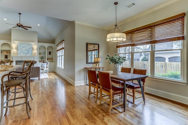 dining room featuring light wood-type flooring, ornamental molding, built in shelves, vaulted ceiling, and ceiling fan