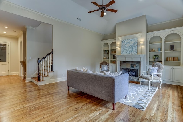 living room featuring a tile fireplace, ceiling fan, built in features, light hardwood / wood-style floors, and vaulted ceiling