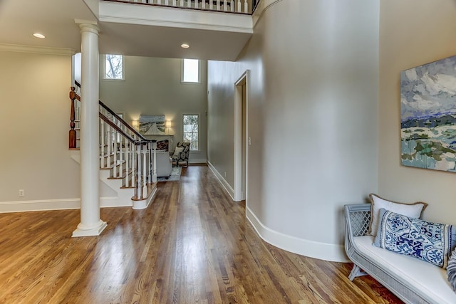 foyer entrance with hardwood / wood-style flooring, a towering ceiling, crown molding, and ornate columns