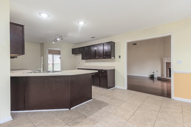 kitchen with dark brown cabinets, light tile patterned flooring, kitchen peninsula, and sink