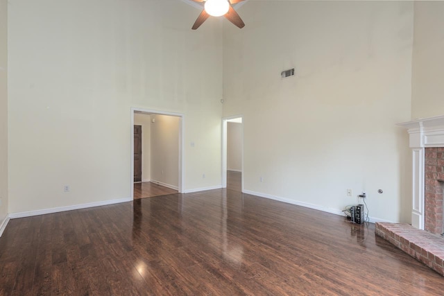 unfurnished living room with ceiling fan, dark hardwood / wood-style flooring, a fireplace, and a high ceiling