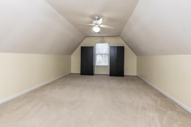 additional living space featuring ceiling fan, light colored carpet, lofted ceiling, and a textured ceiling