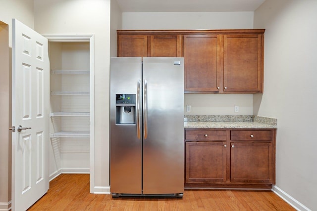 kitchen featuring stainless steel fridge, light stone counters, and light hardwood / wood-style flooring