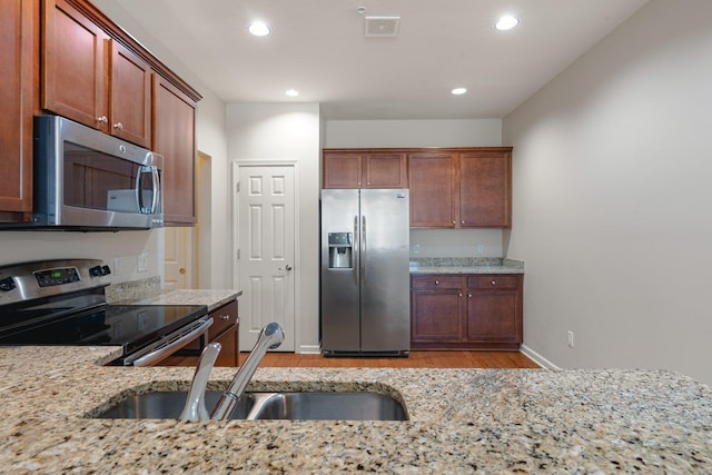 kitchen featuring light stone countertops, sink, light wood-type flooring, and appliances with stainless steel finishes