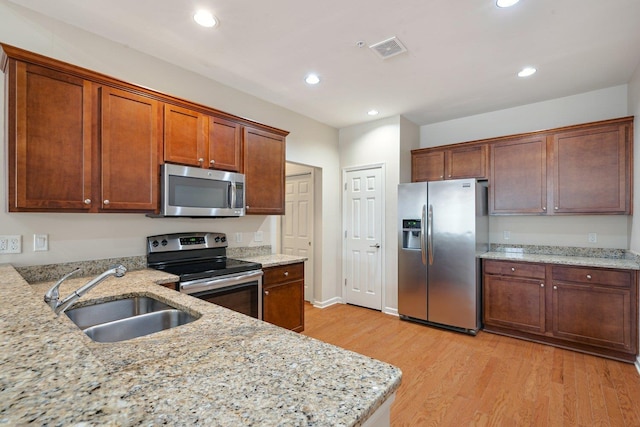 kitchen with stainless steel appliances, light stone counters, light hardwood / wood-style floors, and sink