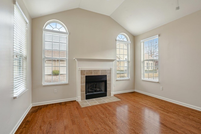 unfurnished living room featuring hardwood / wood-style floors, a tile fireplace, and vaulted ceiling