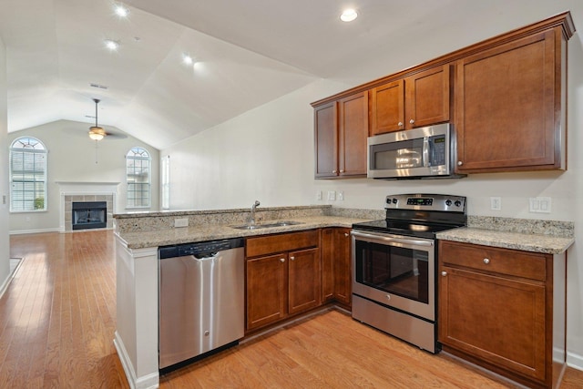 kitchen with sink, vaulted ceiling, ceiling fan, appliances with stainless steel finishes, and a tiled fireplace