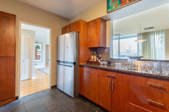 kitchen with dark stone counters, stainless steel fridge, and hanging light fixtures