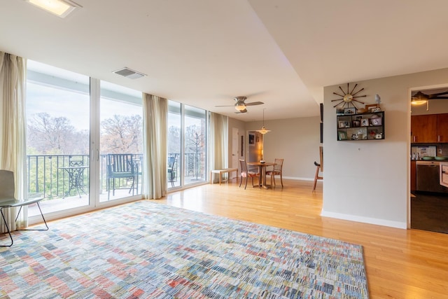 unfurnished living room featuring ceiling fan, a wall of windows, and light hardwood / wood-style flooring