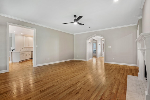 unfurnished living room featuring ceiling fan, sink, ornamental molding, and light wood-type flooring