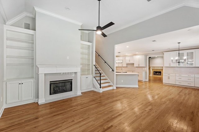 unfurnished living room featuring ceiling fan with notable chandelier, sink, light hardwood / wood-style flooring, ornamental molding, and a fireplace