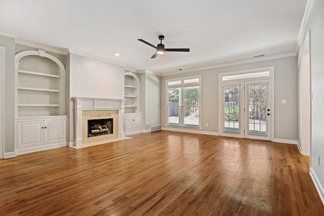 unfurnished living room with built in shelves, ceiling fan, crown molding, and hardwood / wood-style flooring