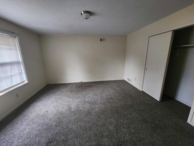 unfurnished bedroom featuring multiple windows, a textured ceiling, dark carpet, and a closet