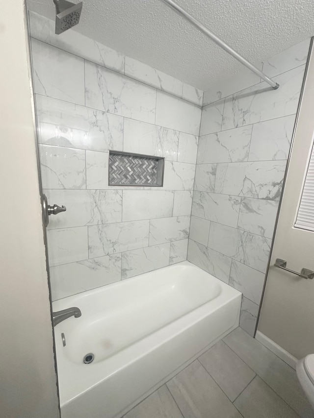 bathroom with tile patterned flooring, tiled shower / bath combo, toilet, and a textured ceiling