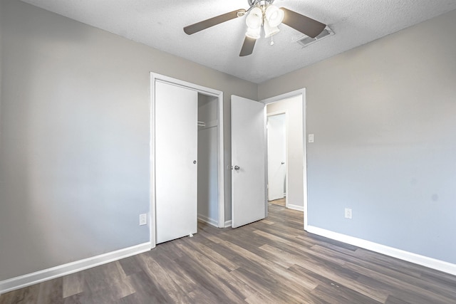 unfurnished bedroom with ceiling fan, a closet, dark wood-type flooring, and a textured ceiling