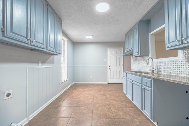 kitchen featuring backsplash, light stone counters, light tile patterned floors, and sink