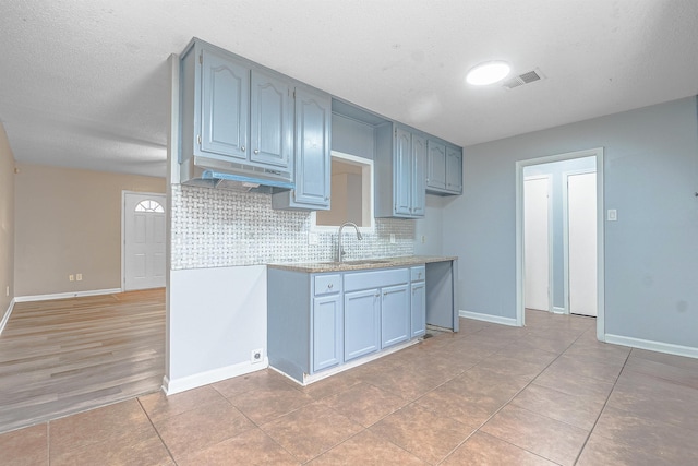 kitchen with decorative backsplash, sink, light tile patterned floors, and a textured ceiling