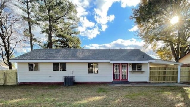 rear view of house with central AC unit and a lawn