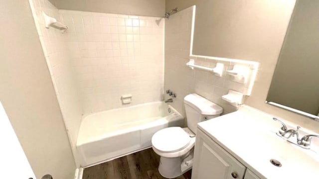 full bathroom featuring vanity, hardwood / wood-style flooring, tiled shower / bath combo, toilet, and tile walls