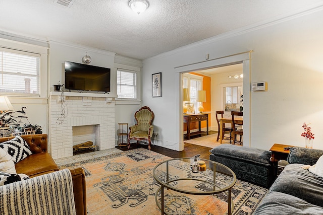 living room with a brick fireplace, hardwood / wood-style flooring, a textured ceiling, and ornamental molding