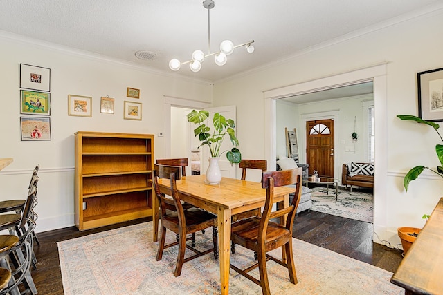 dining room with a textured ceiling, dark wood-type flooring, a notable chandelier, and ornamental molding