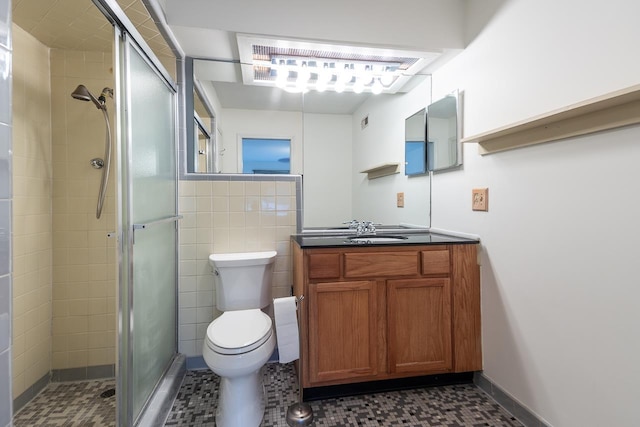 bathroom with vanity, toilet, a shower with door, and tile walls