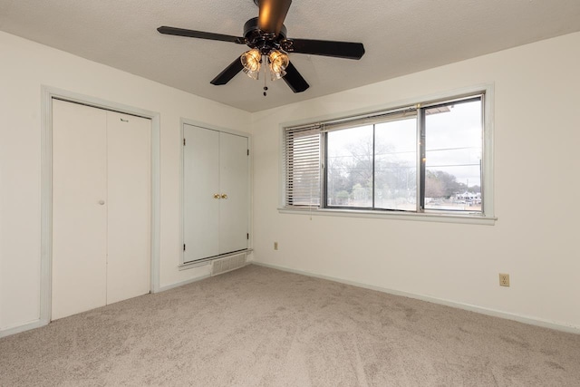 unfurnished bedroom with light carpet, two closets, and ceiling fan