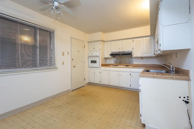 kitchen with oven, sink, ceiling fan, stovetop, and white cabinetry