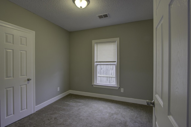 spare room featuring a textured ceiling, dark carpet, visible vents, and baseboards