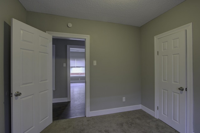 empty room with dark colored carpet, a textured ceiling, and baseboards