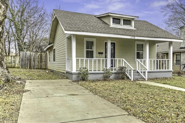 bungalow-style house with covered porch, a shingled roof, and fence