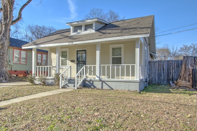 bungalow-style house with a front yard, covered porch, roof with shingles, and fence