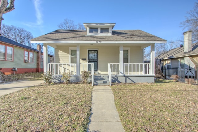 bungalow with covered porch, fence, and a front yard