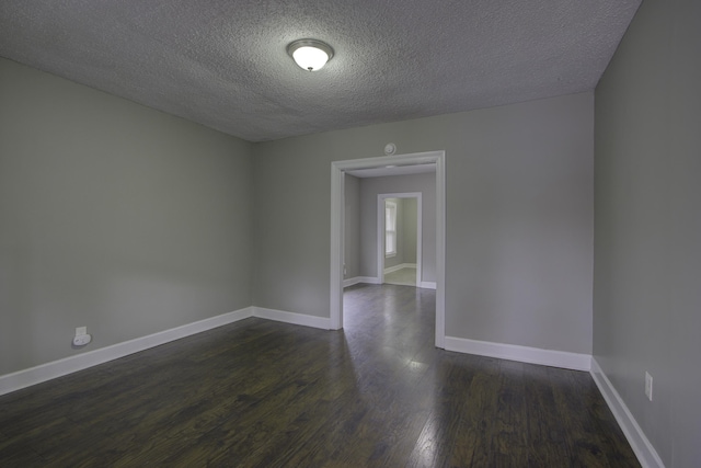 empty room with dark wood-style flooring, a textured ceiling, and baseboards