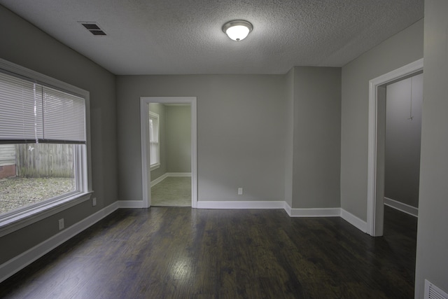 spare room featuring a textured ceiling, dark wood-style flooring, visible vents, and baseboards