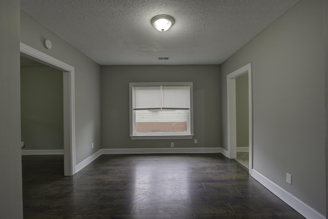 empty room featuring a textured ceiling, dark wood finished floors, visible vents, and baseboards