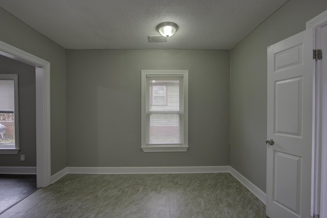 spare room featuring baseboards, visible vents, and a textured ceiling