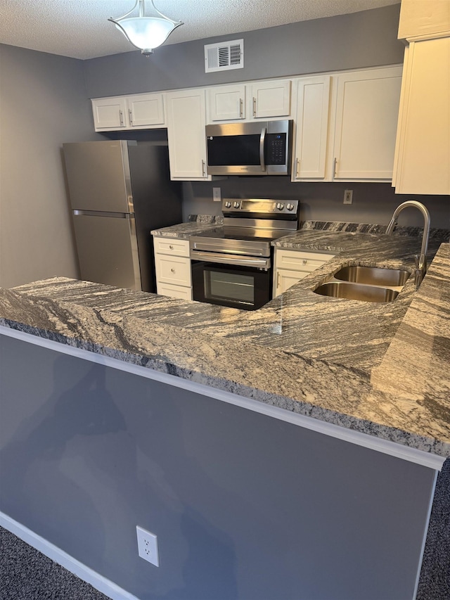 kitchen with white cabinets, sink, a textured ceiling, kitchen peninsula, and stainless steel appliances