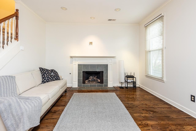 living room featuring a tiled fireplace, crown molding, and dark hardwood / wood-style floors