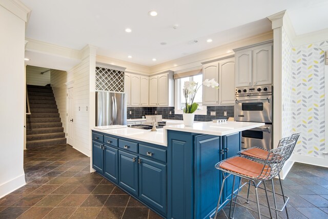 kitchen featuring appliances with stainless steel finishes, backsplash, a breakfast bar, blue cabinetry, and a kitchen island