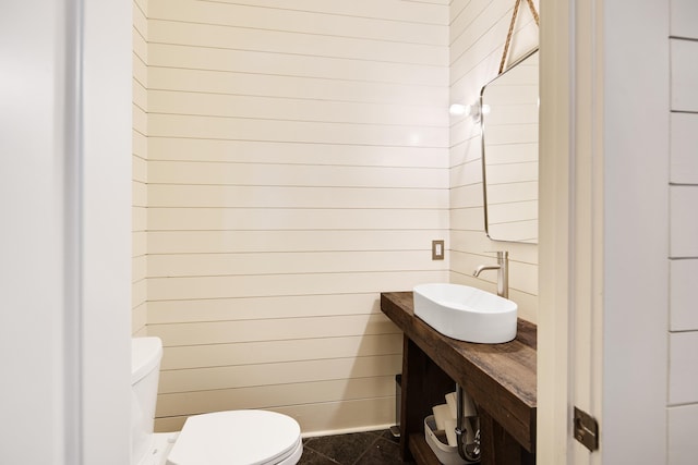 bathroom featuring tile patterned flooring, wood walls, toilet, and sink