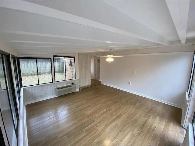 unfurnished living room with a wall mounted air conditioner, ceiling fan, beam ceiling, and hardwood / wood-style flooring