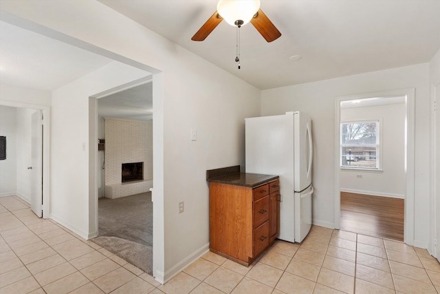 kitchen with white fridge, a brick fireplace, ceiling fan, and light tile patterned flooring