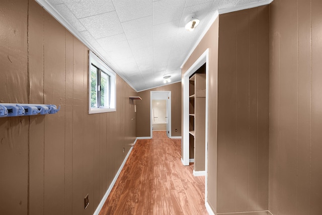 hallway featuring vaulted ceiling, light hardwood / wood-style flooring, crown molding, and wood walls