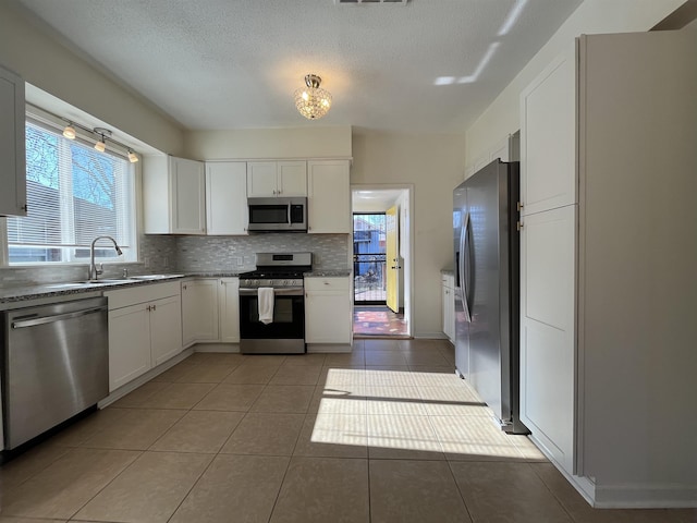 kitchen with backsplash, sink, tile patterned flooring, white cabinetry, and stainless steel appliances