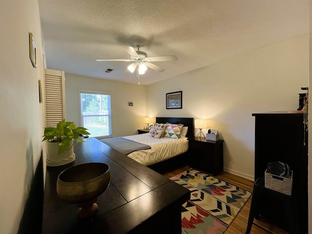 bedroom with ceiling fan, wood-type flooring, and a textured ceiling