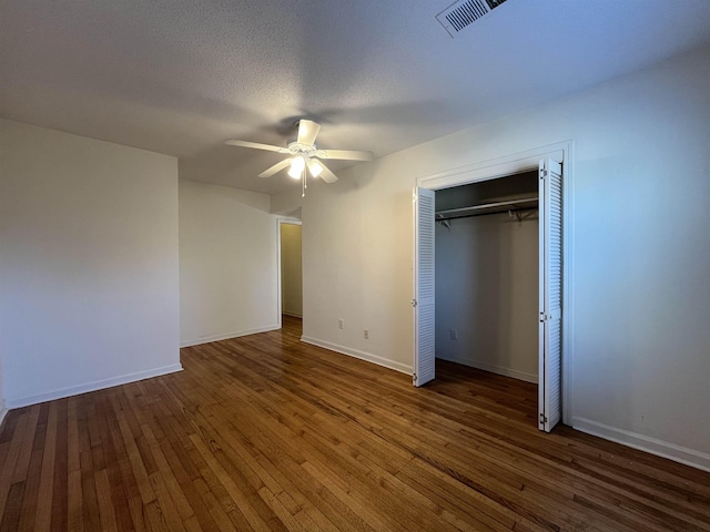 unfurnished bedroom featuring a textured ceiling, dark hardwood / wood-style flooring, a closet, and ceiling fan