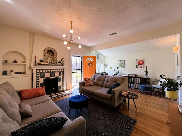 living room with built in shelves, a textured ceiling, wood-type flooring, a notable chandelier, and a tiled fireplace