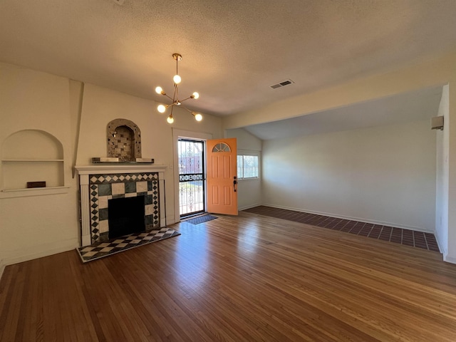 unfurnished living room with lofted ceiling, built in features, a fireplace, a notable chandelier, and dark hardwood / wood-style flooring